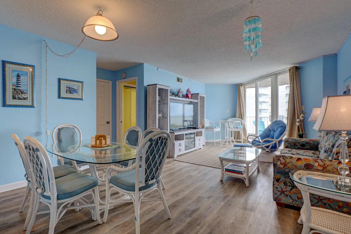 A cozy dining area with a dining table and colorful couch set beside large windows. The windows invite in natural light and offer scenic views, creating a bright and welcoming space for family meals or romantic dinners overlooking the ocean.