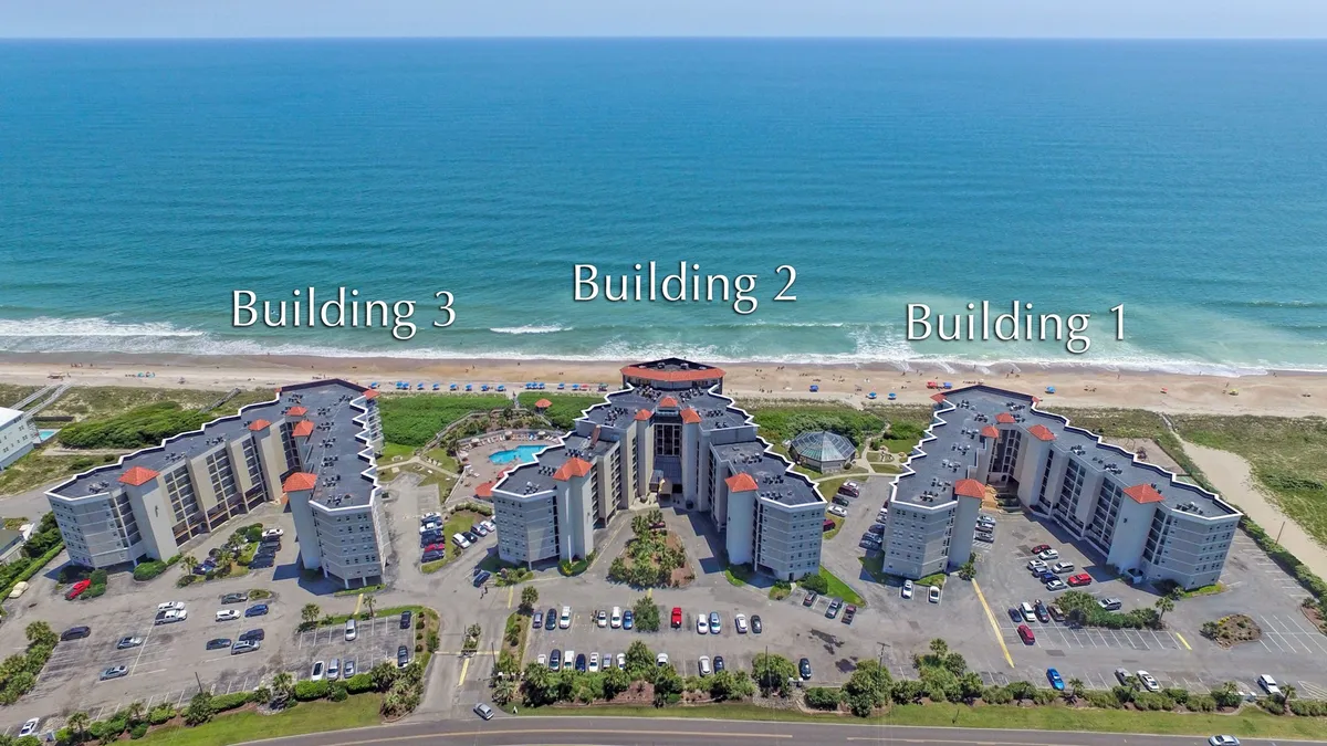 This exterior image captures three resort buildings aligned along a beautiful stretch of beach. The foreground features a sparkling swimming pool area, with the ocean visible just beyond. The setting sun casts a warm glow, and the area invites guests to swim, sunbathe, or stroll along the sand after a productive day.