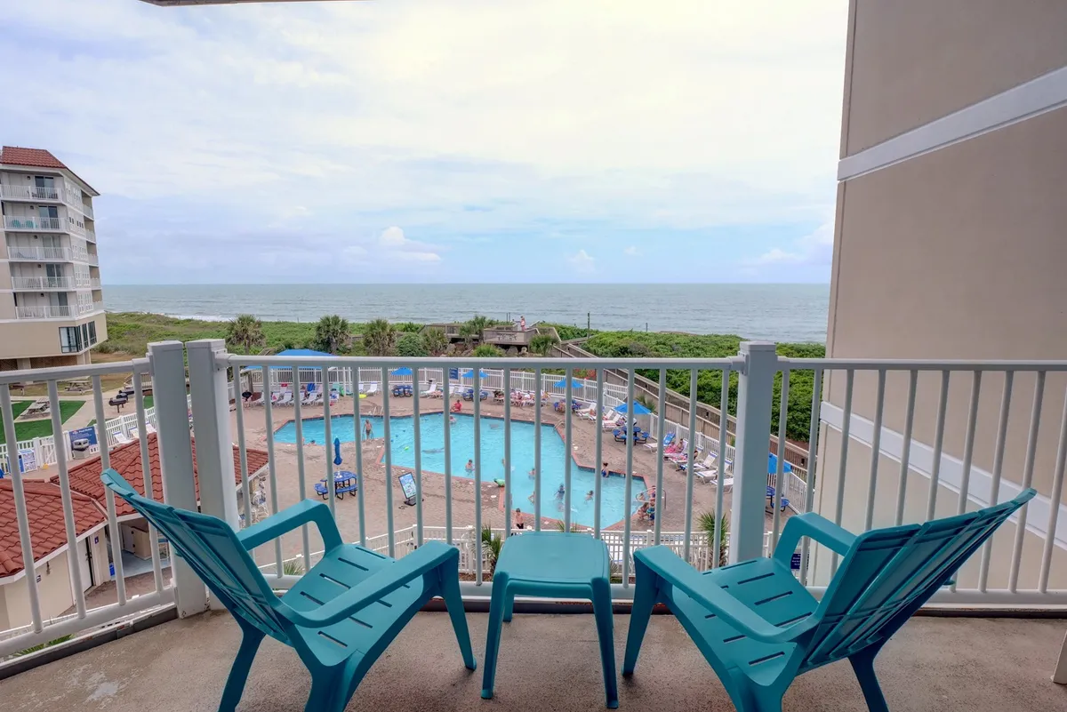 The image showcases a serene balcony overlooking a shimmering saltwater pool, with inviting chairs perfectly positioned to take in sweeping ocean views. The scene suggests relaxation and leisure, highlighting opportunities for sunbathing, swimming, and enjoying breathtaking sunsets or evening conversations beneath the stars.