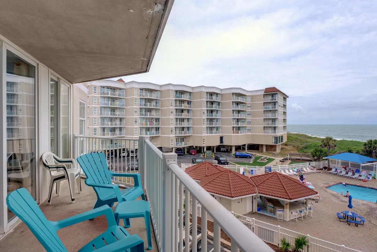 A scenic view from a private balcony overlooks the swimming pool below and offers sweeping ocean vistas. Outfitted with comfortable chairs, the balcony invites relaxation, socializing, and dolphin watching—all within sight of both aquatic fun and tranquil waters.