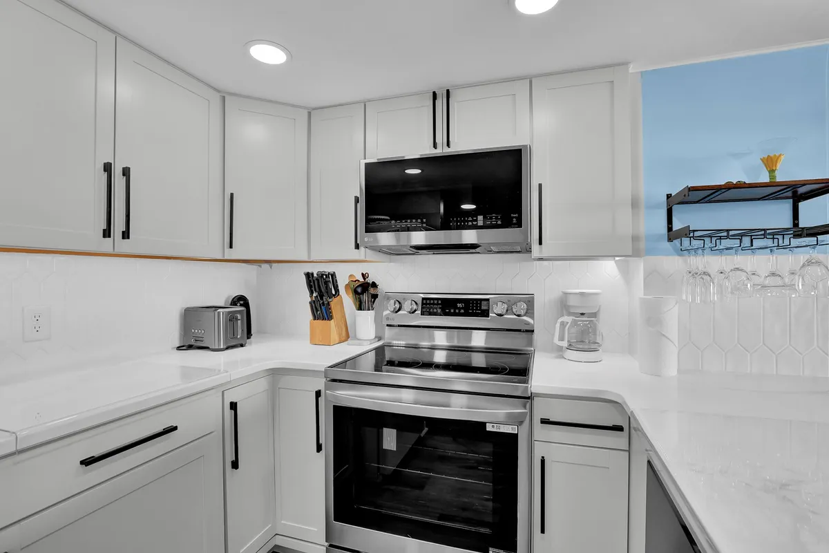 A sleek kitchen space featuring a stainless steel stove, crisp white cabinetry, and a spacious countertop with utensils ready for use. A window offers a pleasant view, enhancing the connection to the coastal setting and providing natural light.
