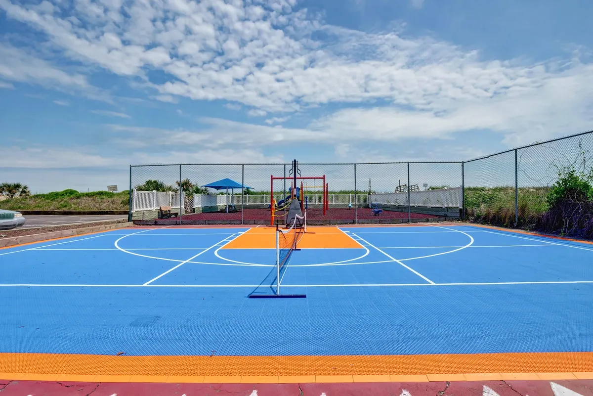 This image showcases an exterior multi-sport court featuring a basketball hoop and tennis net on a colorful court surface. The setting is bright and lively, with plenty of space for outdoor exercise and friendly competition.