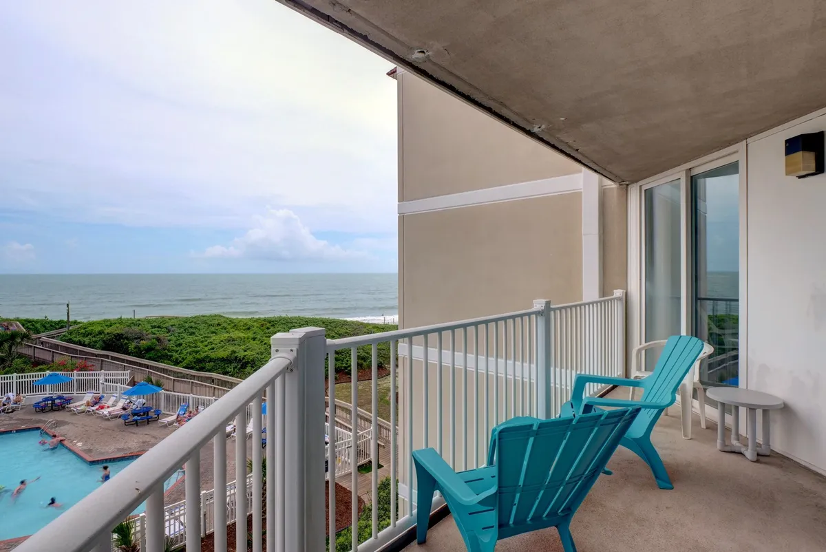 This exterior image features balcony chairs overlooking a stunning ocean view, with a swimming pool visible below. The tranquil setting is perfect for relaxing, reading, or simply taking in the panoramic seascape.