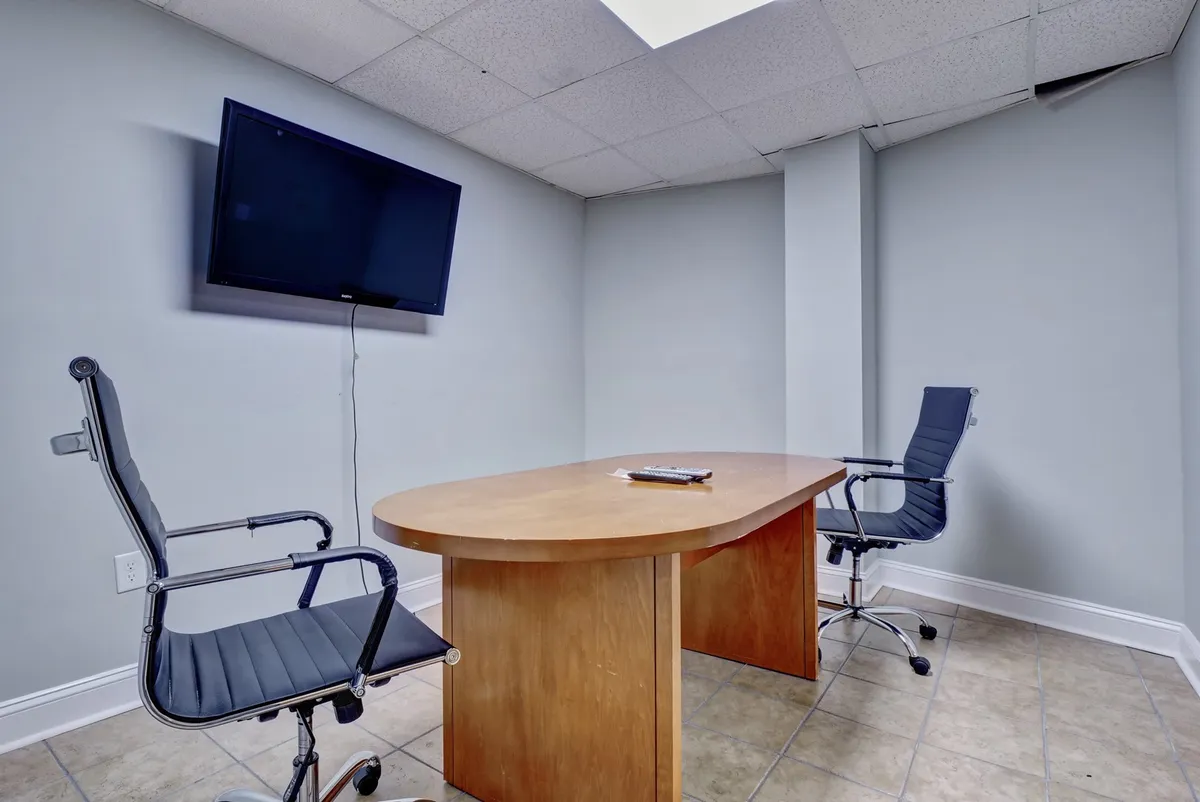 An interior conference room set-up with a table, chairs, and a large TV screen. The space is clearly designed for business meetings, discussions, or presentations, emphasizing a professional atmosphere conducive to remote work.